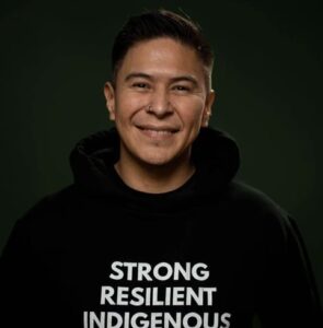 Photo of Len Pierre, a youthful indigenous man wearing a black hoodie with text that reads, "Strong Resilient Indigenous"