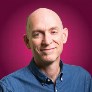 A head shot of David Lee King in front of a purple background. David is wearing a blue button up shirt, he is white, middle-aged, smiling and without hair.