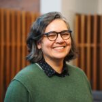 A headshot of Mita Williams, the Law Librarian at University of Windsor. Mita is smiling, wearing glasses, and has shoulder length hair that is dark with gray. She wears a green sweater and her complexion is light.